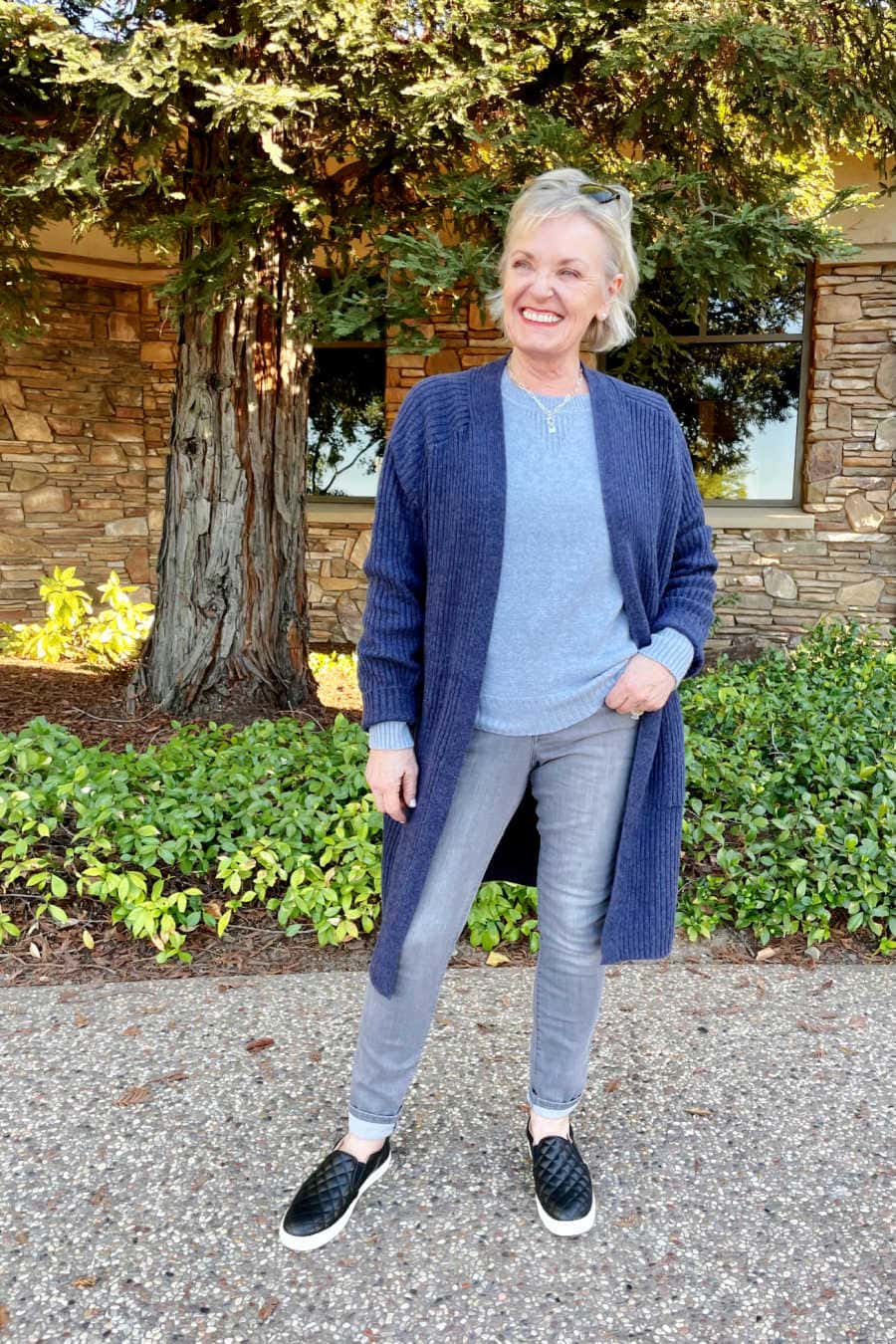 woman wearing blue sweaters and gray jeans with black quilted sneakers