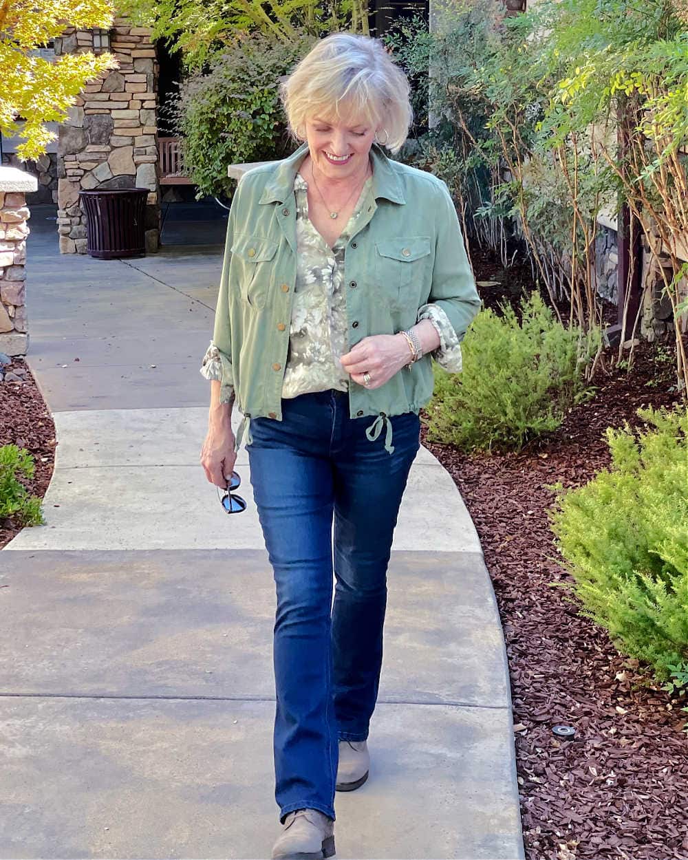 blond woman walking in itty bitty bootcut jeans and green jacket