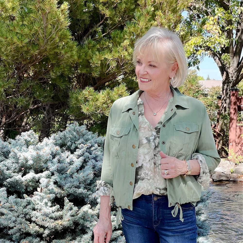 BLONDE WOMAN WEARING FLORAL SHIRT AND GREEN ULTILITY JACKET FOR WARM FALL TEMP