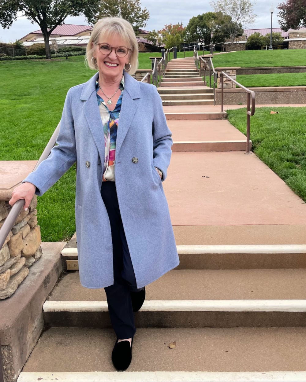 woman walking down stairs in blue coat and floral blouse