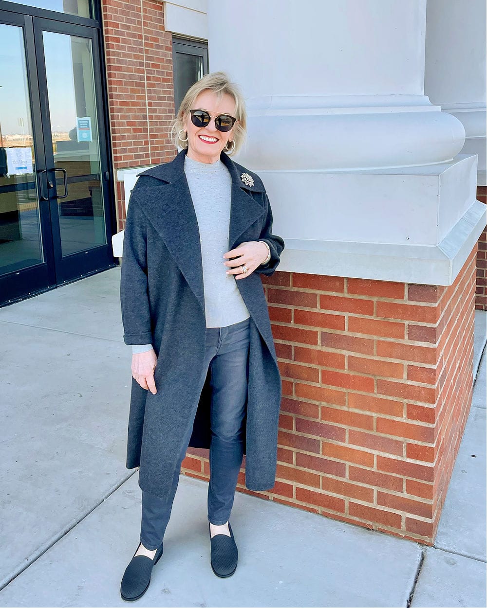 woman standing by white pillar wearing gray outfit