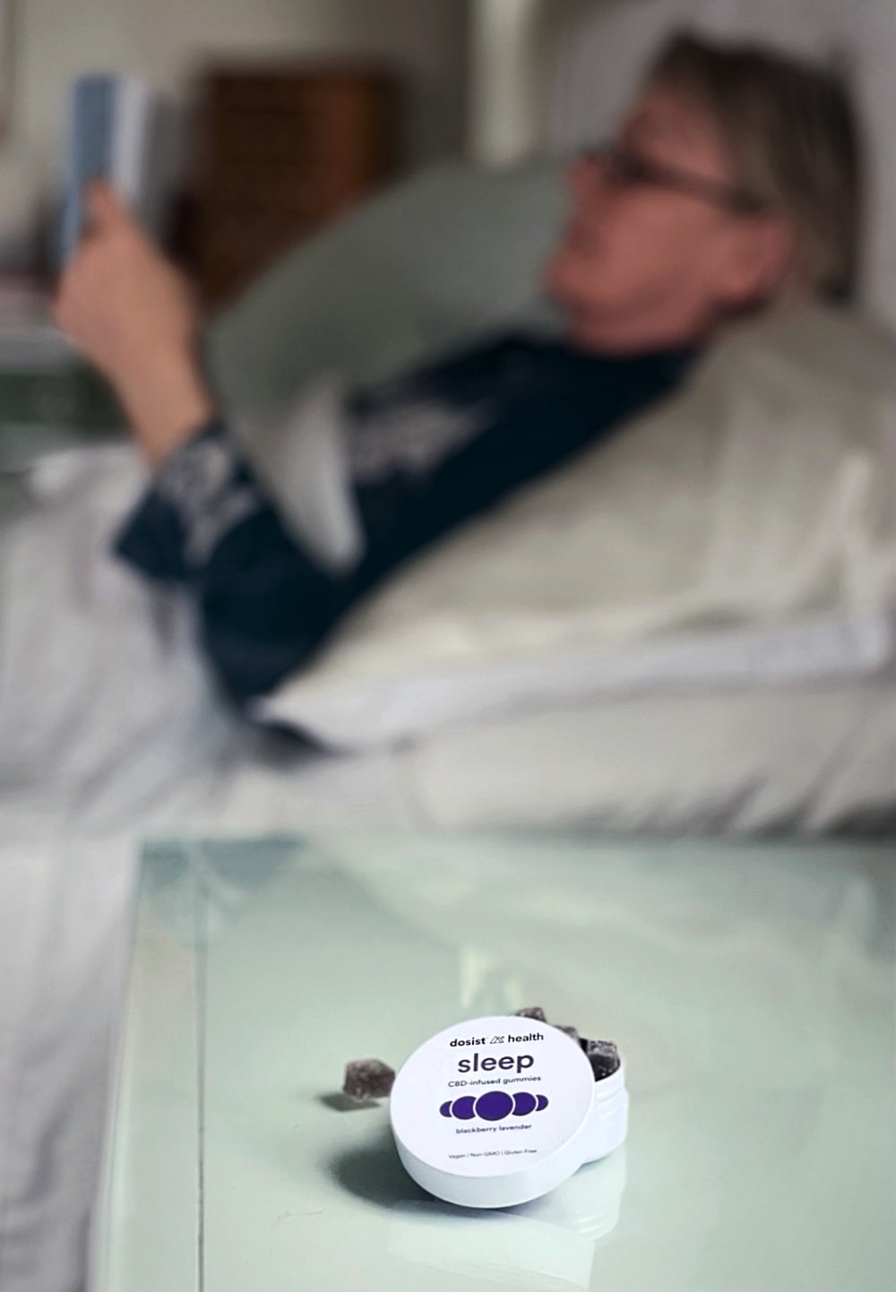woman reading in bed with CBD gummies on table