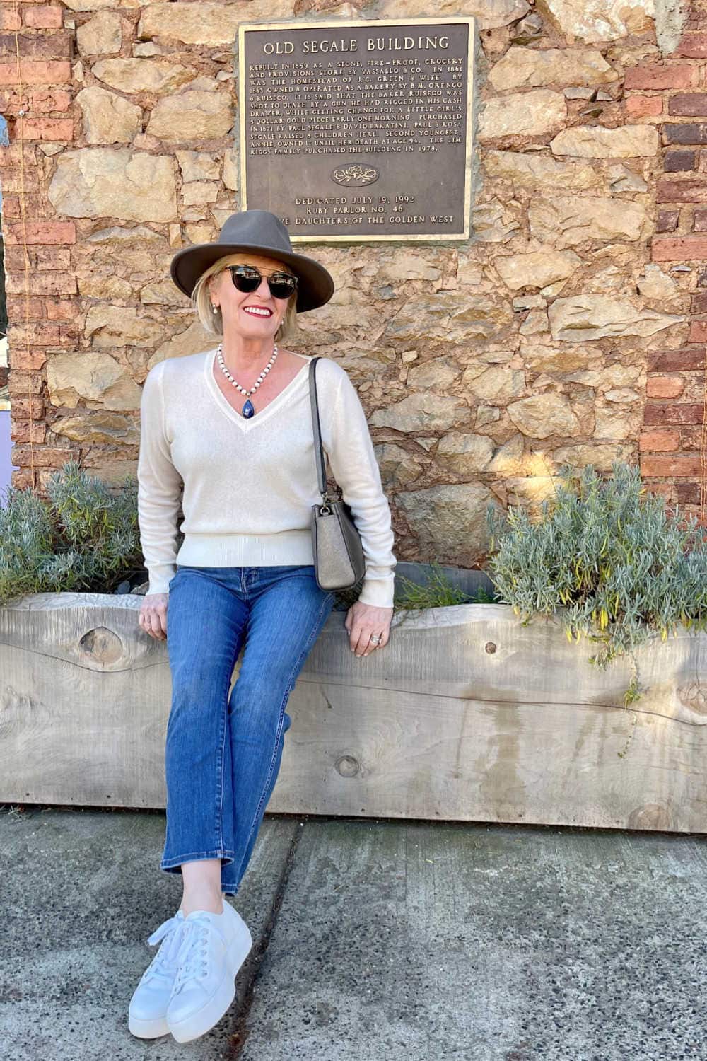 WOMAN WEARING JEANS AND IVORY SWEATER SITTING ON WALL visting murphy's and the giant sequoia trees