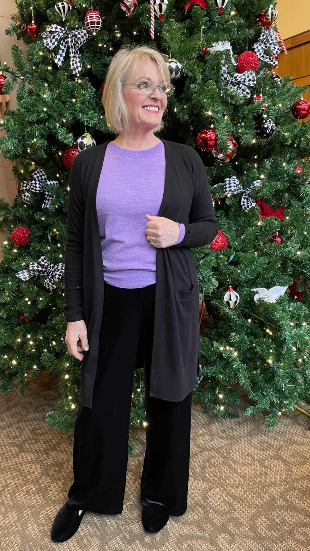 woman standing in front of christmas tree wearing casual festive outfit