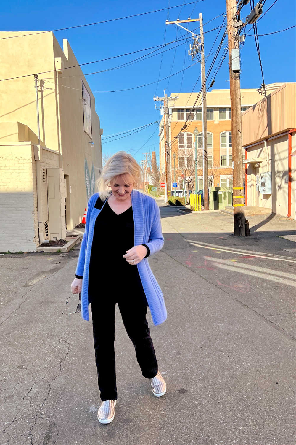 blonde woman walking in alley in blue cardigan