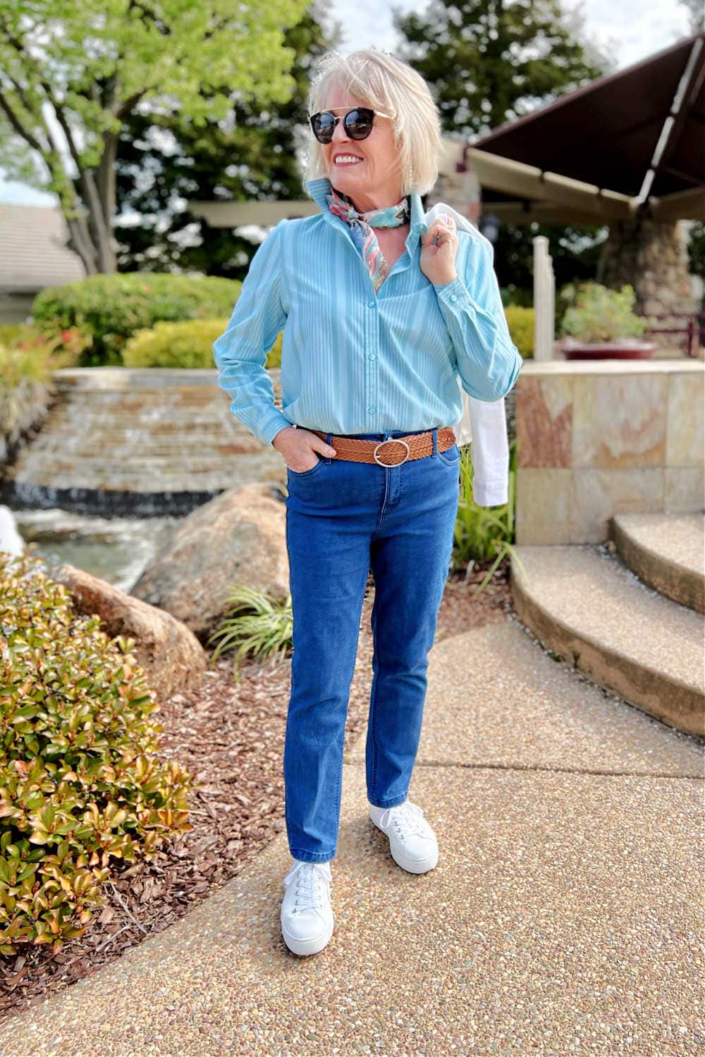 woman standing in front of fountain wearing stiped shirt and blue jeans