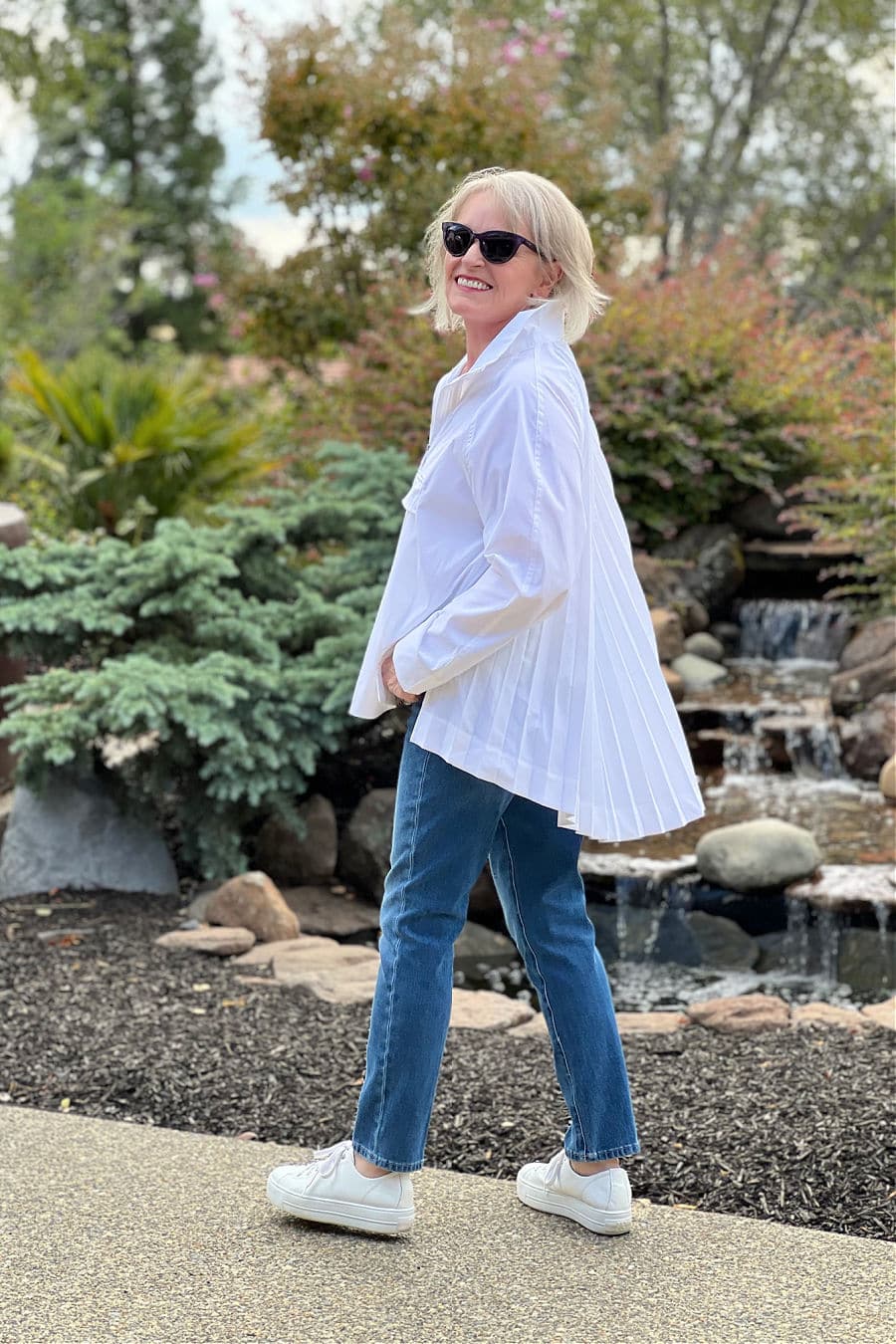 over 50 blogger jennifer connolly wearing athelta sojourn white shirt and blue jeans in front of water fountain