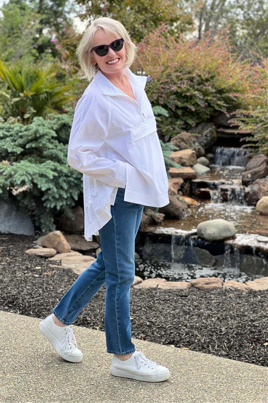 women wearing athleta sojourn top with blue jeans and white sneakers