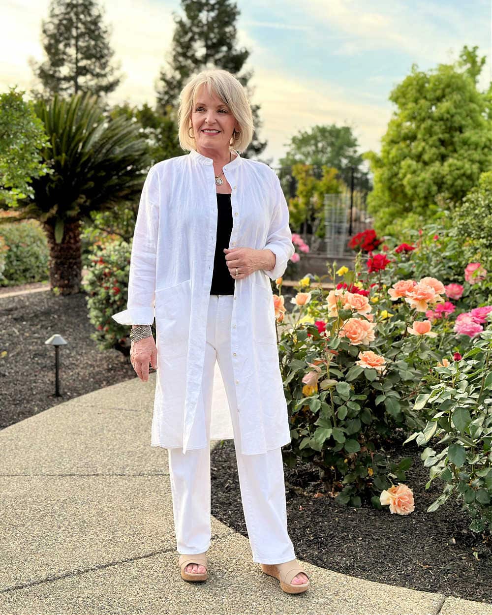 woman wearing eileen fisher white linen shirtdress open over black tank top and white mother jeans