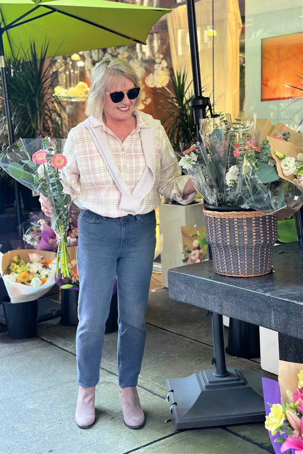 woman buying flowers wearing booties, flannel shirt, gray jeans with sweater over shoulders fall fashion from kohls