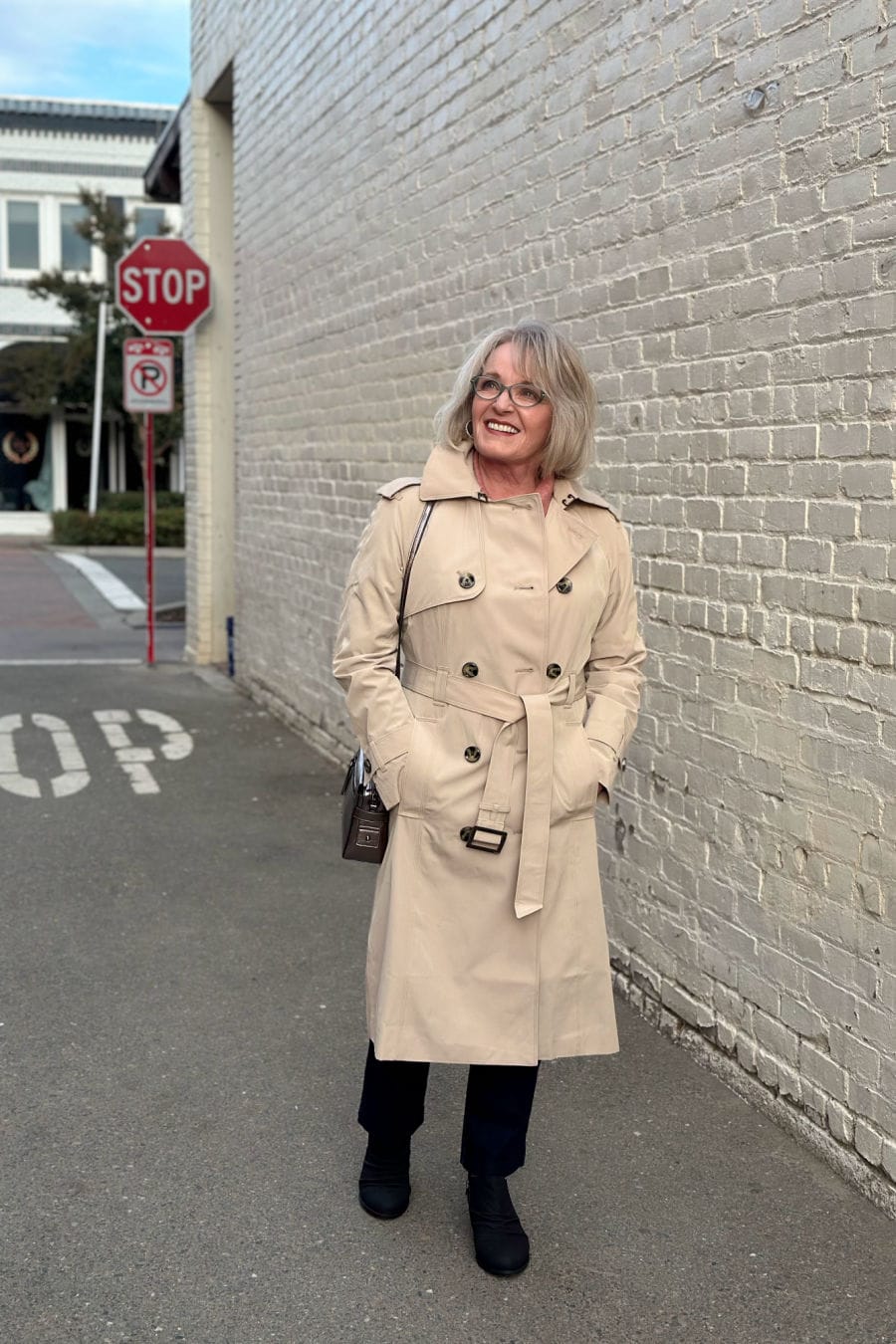 over 50 woman walking in alley wearing beige coat and dark pants
