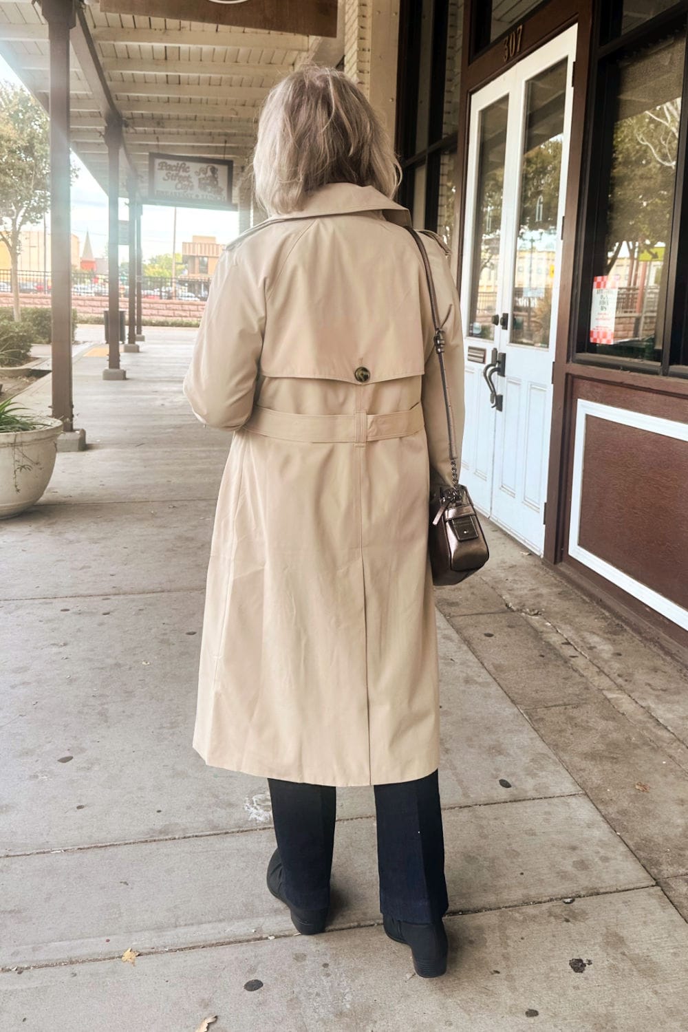 back of woman in sidewalk wearing trench coat