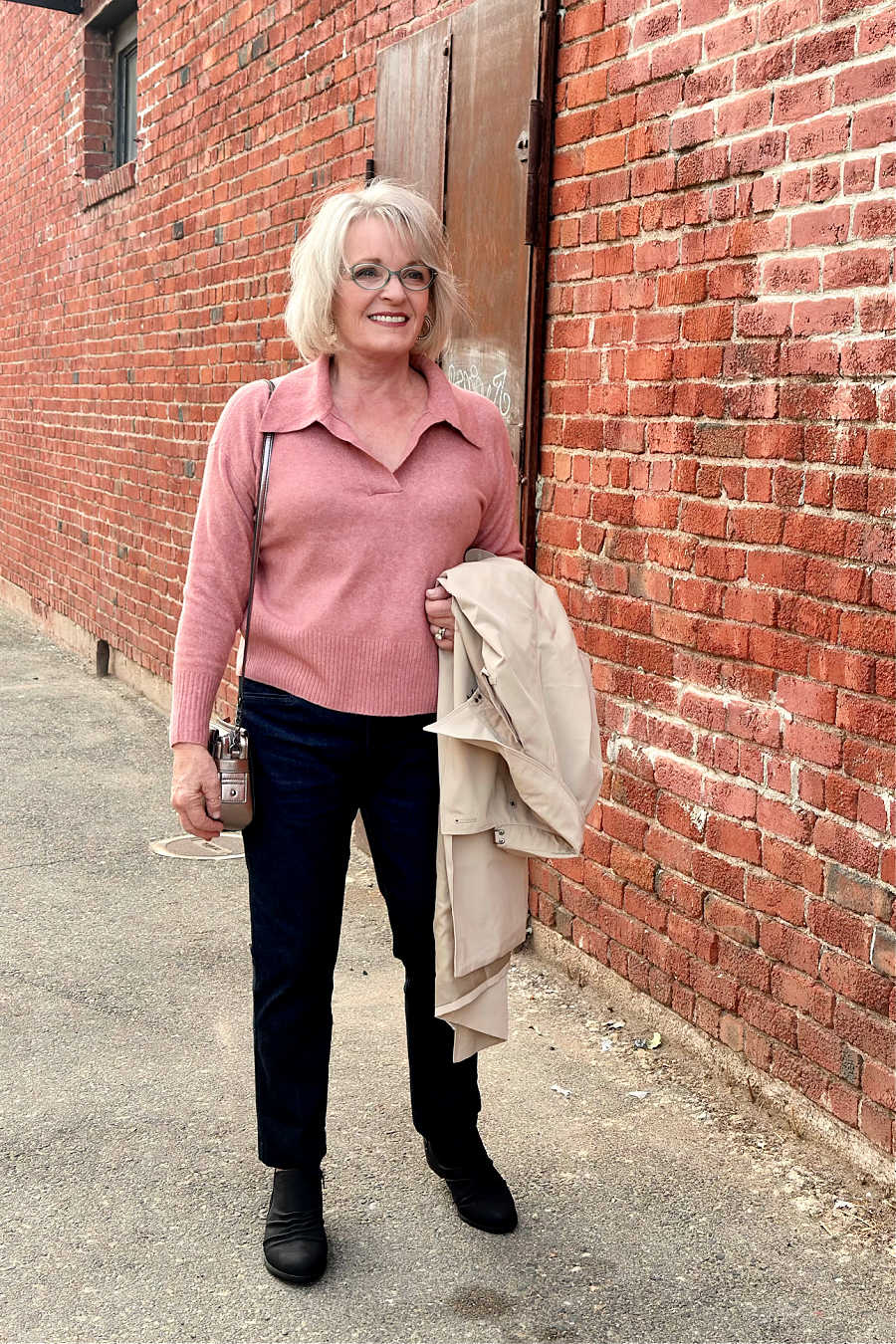 woman wearing pink sweater dark pants and carrying trench coat
