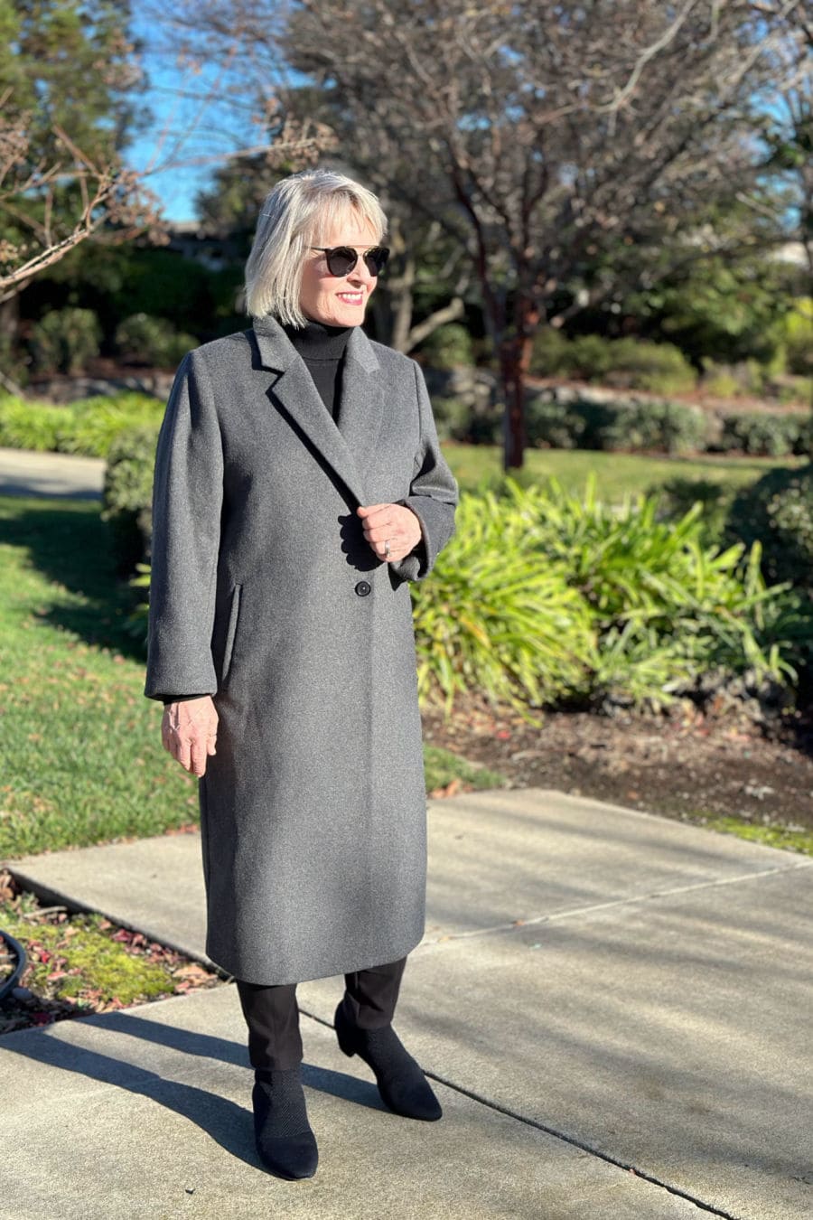 woman wearing long gray quince wool coat over black turtleneck and slim pants