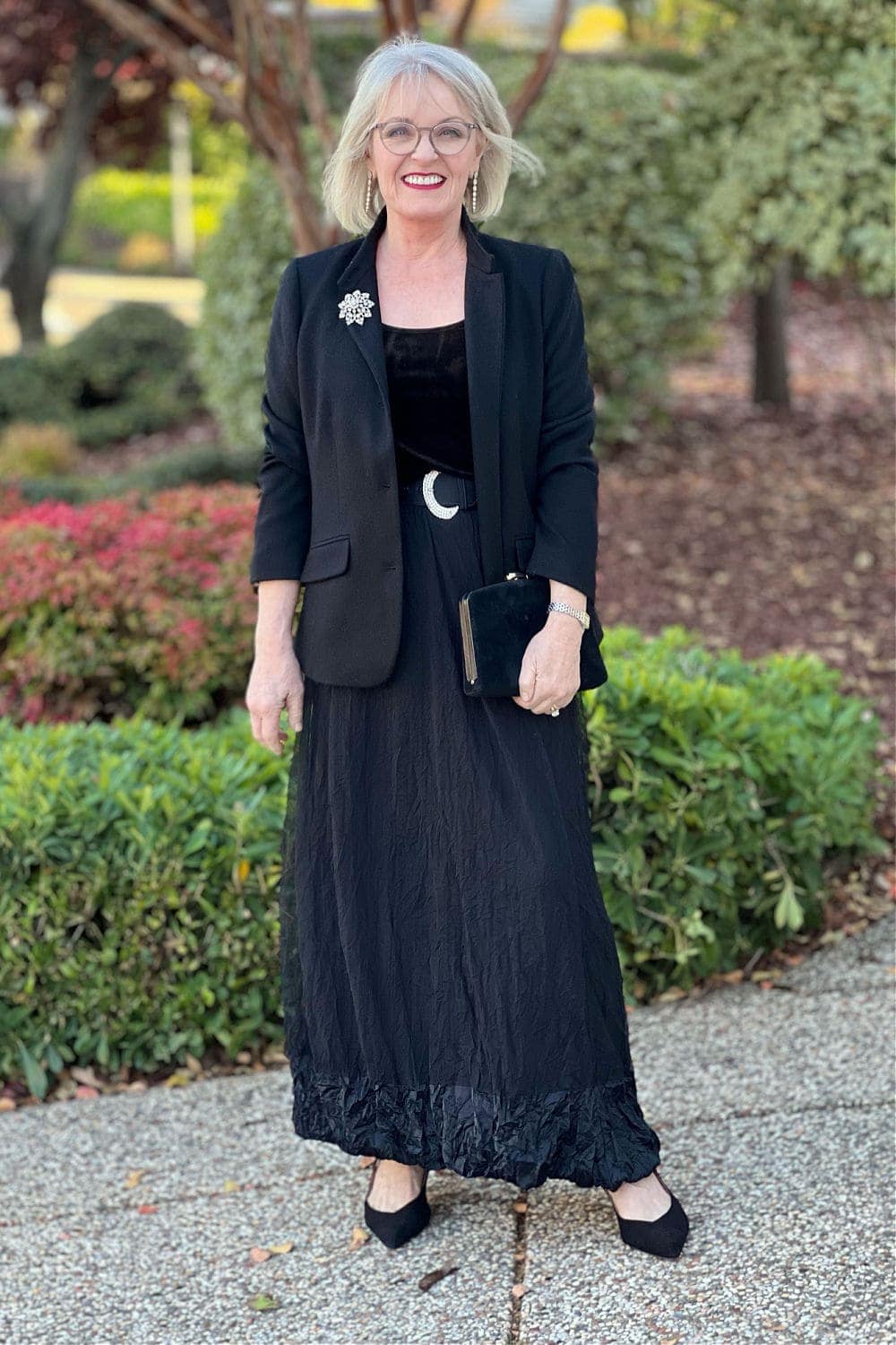 older woman in long gauze skirt, black blazer, unique broach and belt