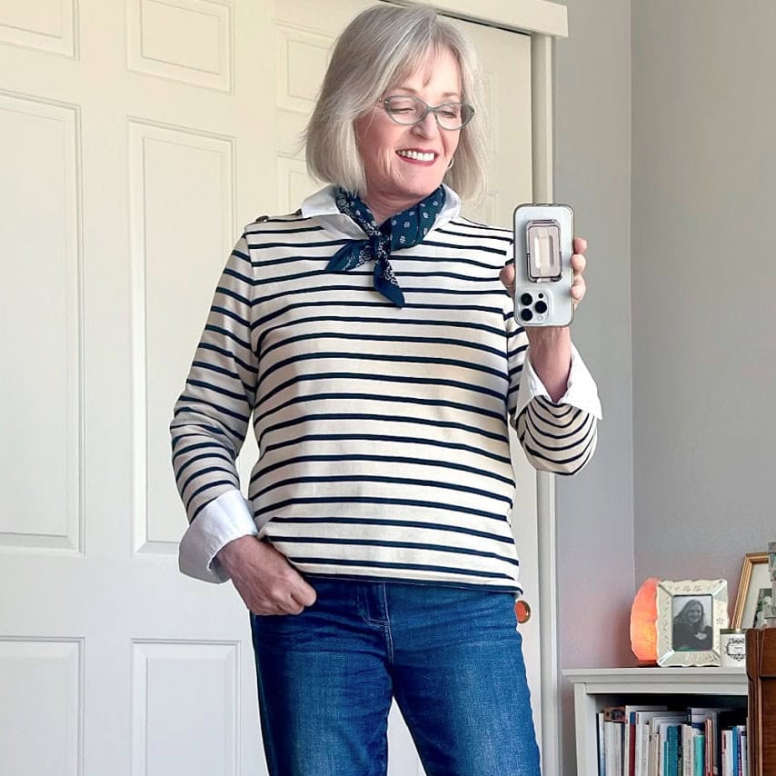older woman wearing breton strip top trend for 2024 with blue jeans and neck scarf