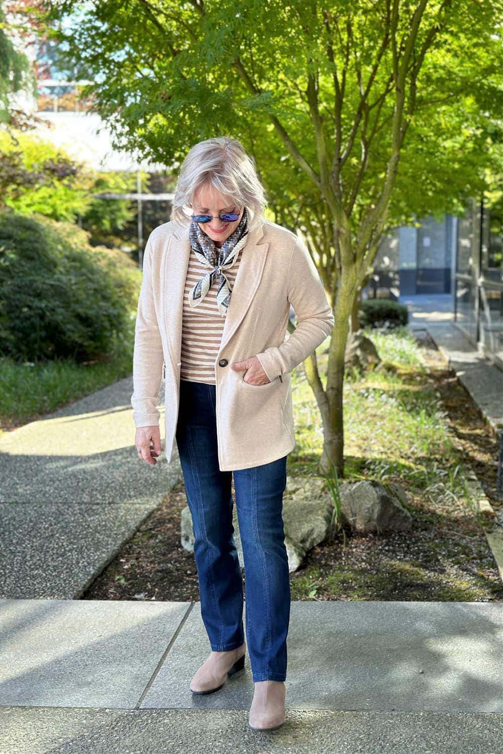 Fresh fall look with a cream knit blazer, striped tee, dark jeans, and taupe booties on a woman over 60.