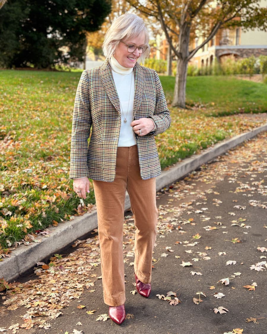 Woman over 60 wearing a checked blazer with a cream turtleneck, camel trousers, and burgundy heels.