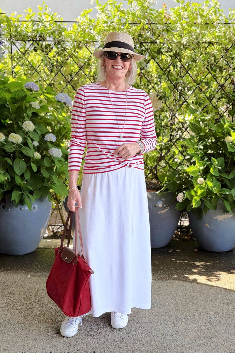Simple white dress layered with striped t-shirt, red tote, and sneakers for a colorful summer look over 60