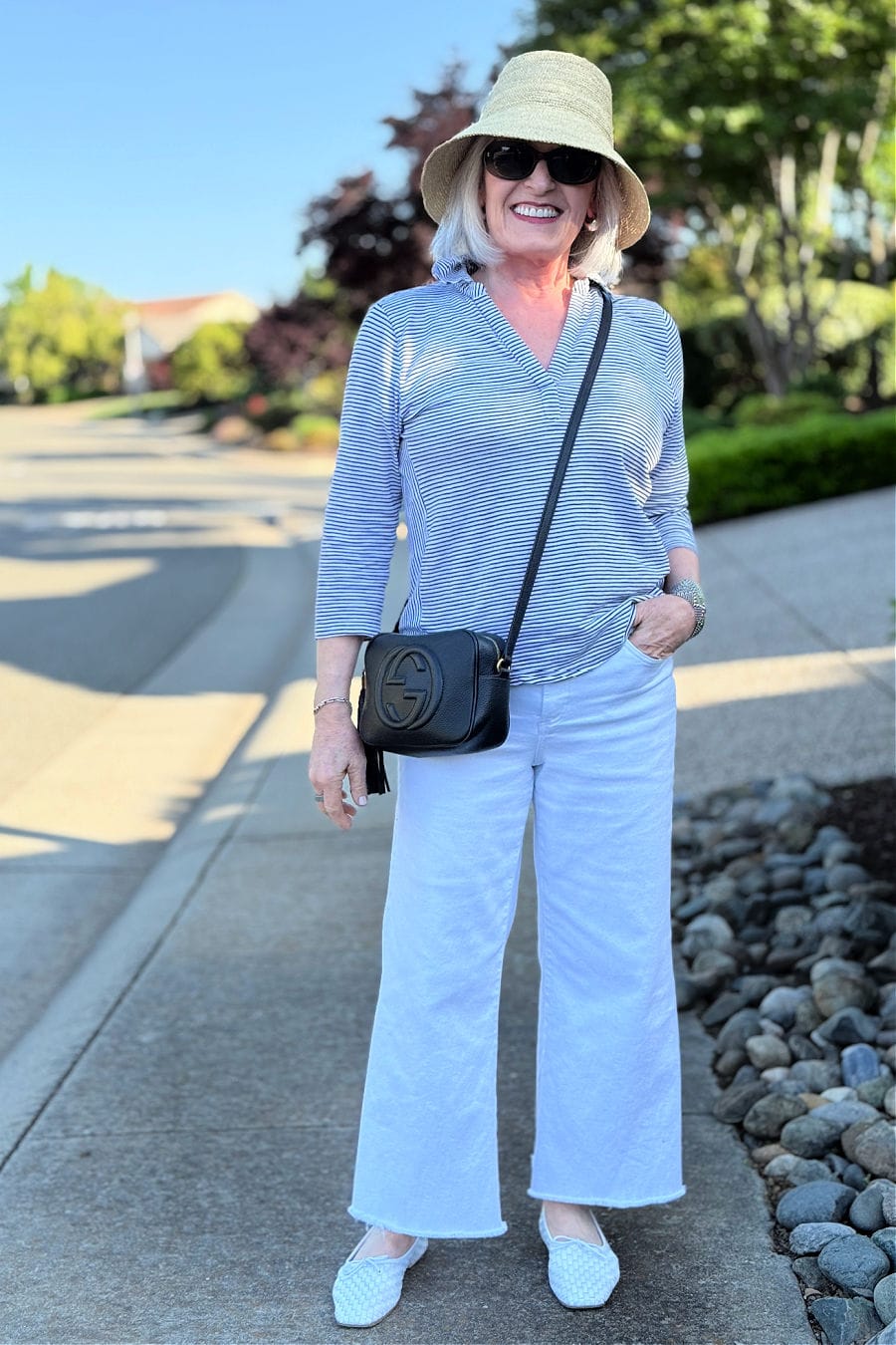 over 60 woman wearing casual spring outfit with striped tee and white jeans wearing a bucket hat