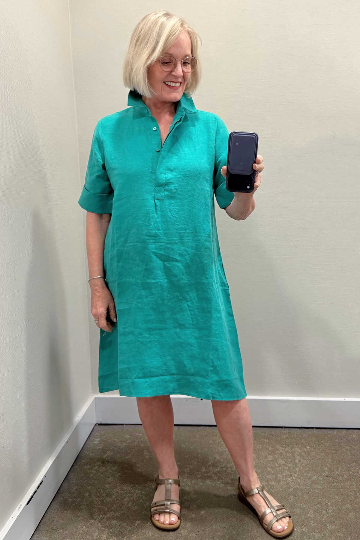 Jennifer Connolly wearing a teal green linen shirt dress with metallic sandals, styled as an easy summer dress for women over 60.