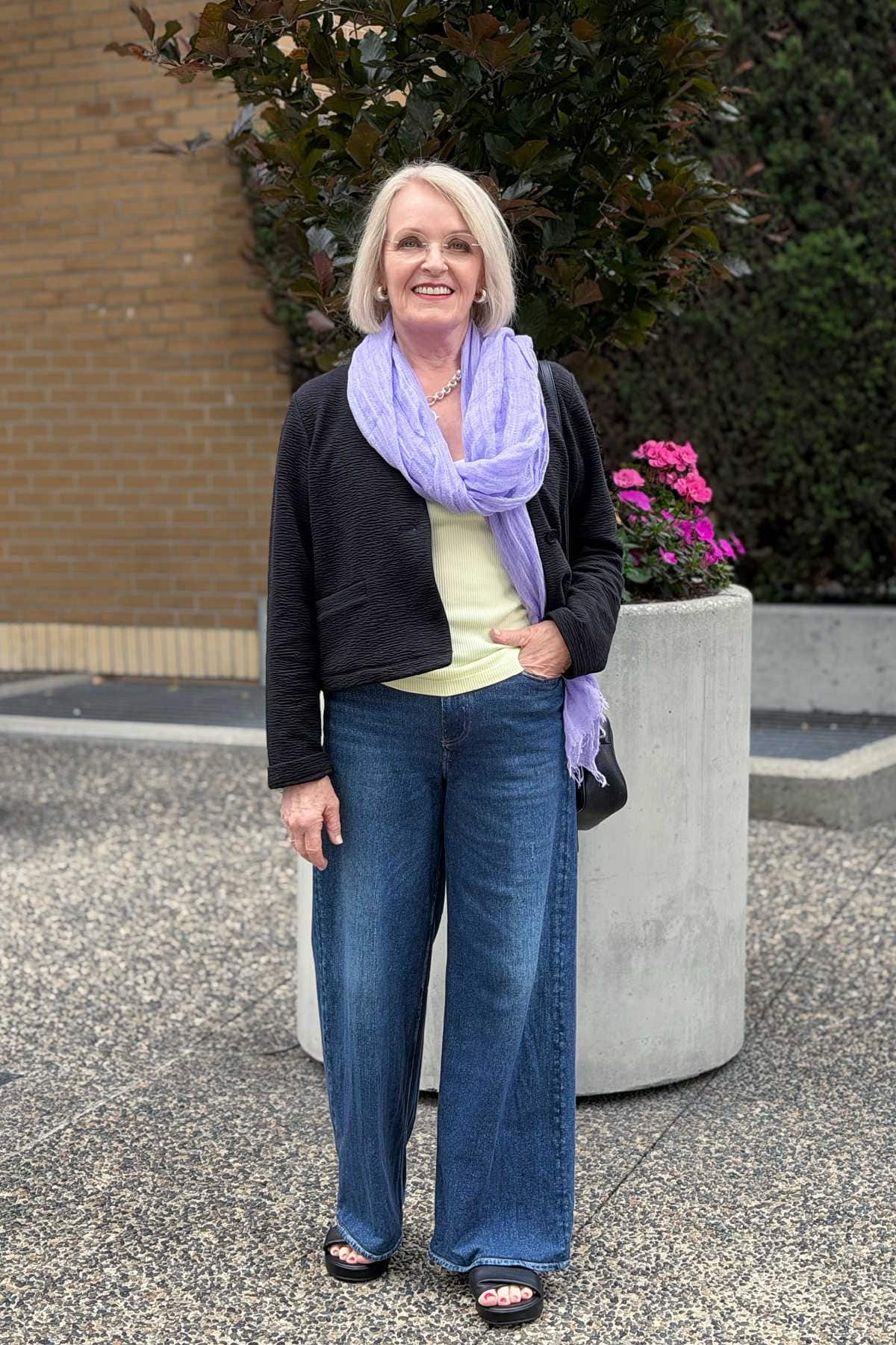 older woman wearing wide leg jeans with a cropped jacket or the best proportion and lavender scarf liime colors tank top
